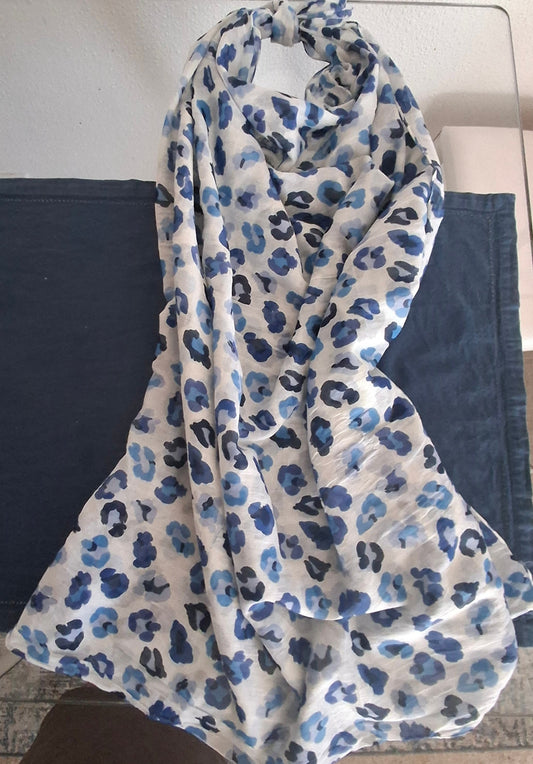 A lightweight white scarf with a blue and navy leopard print pattern, draped over a dark blue fabric surface.