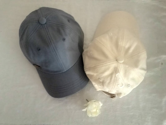 Two baseball caps, one gray and one beige, on a light surface.