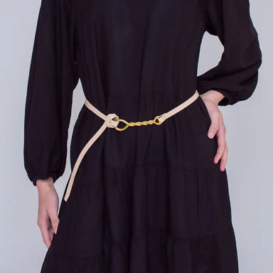 Person wearing a navy dress with a narrow leather belt, sporting fashionable gold-tie buckle on a plain background