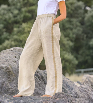 Person wearing beige pants with a white top on a rocky surface with greenery in the background