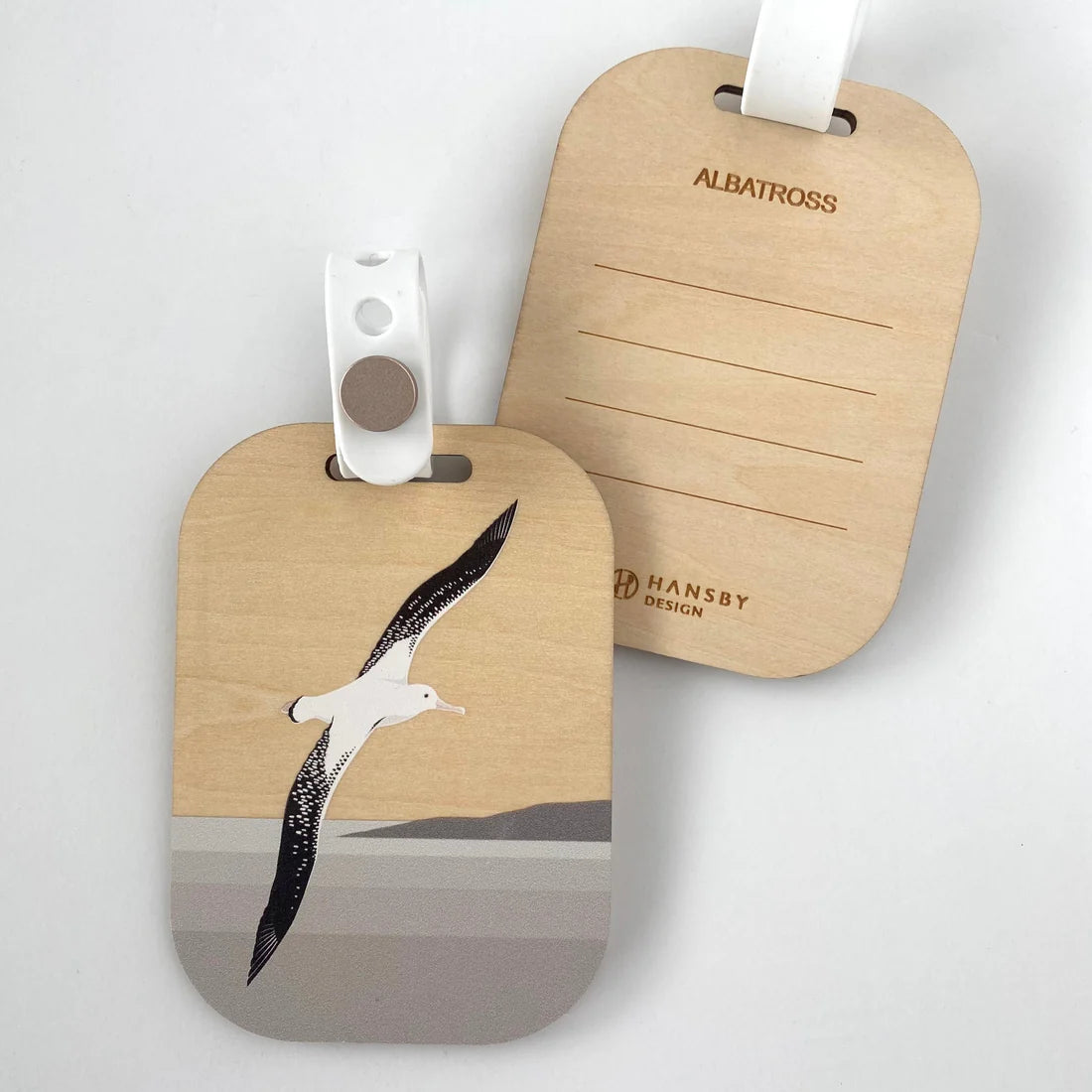 Two wooden luggage tags showing both sides of one typical tag - with paint-printed 'Albatross'  design on one ; and 'Albatross' branding on a light gray background with lines to write on, on other - both with tag attachments.