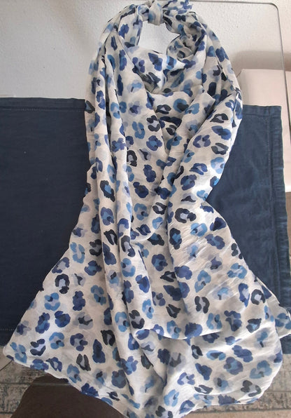 A lightweight white scarf with a blue and navy leopard print pattern, draped over a dark blue fabric surface.