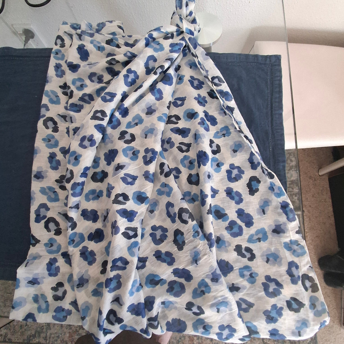 A lightweight white wrap or shawl with a blue and navy leopard print pattern, draped over dark blue fabric laid flat.