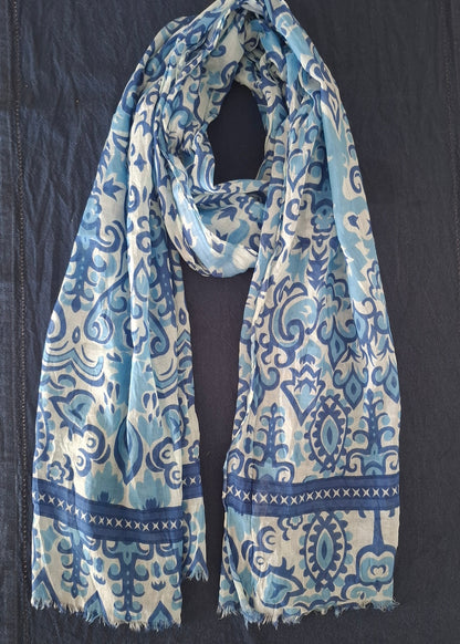 A lightweight scarf with a blue and white traditional pattern, laid flat on a dark navy blue fabric surface.