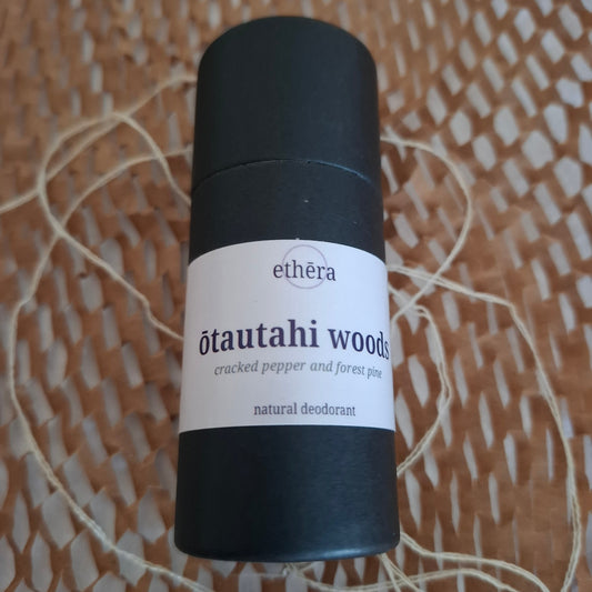 A black cylindrical deodorant stick with a white label reading 'ethéra ōtautahi woods cracked pepper and pine peat natural deodorant', placed on a woven brown surface with string.