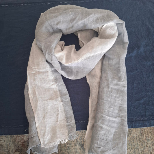 A light blue linen scarf with frayed edges, draped in a loose loop over a dark blue fabric surface.