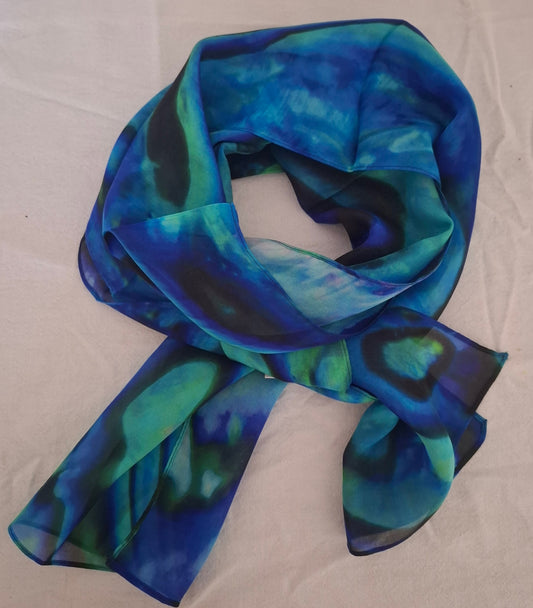 A lightweight scarf with an abstract marbled pattern in shades of blue, teal, and dark navy, laid out on a white fabric background.
