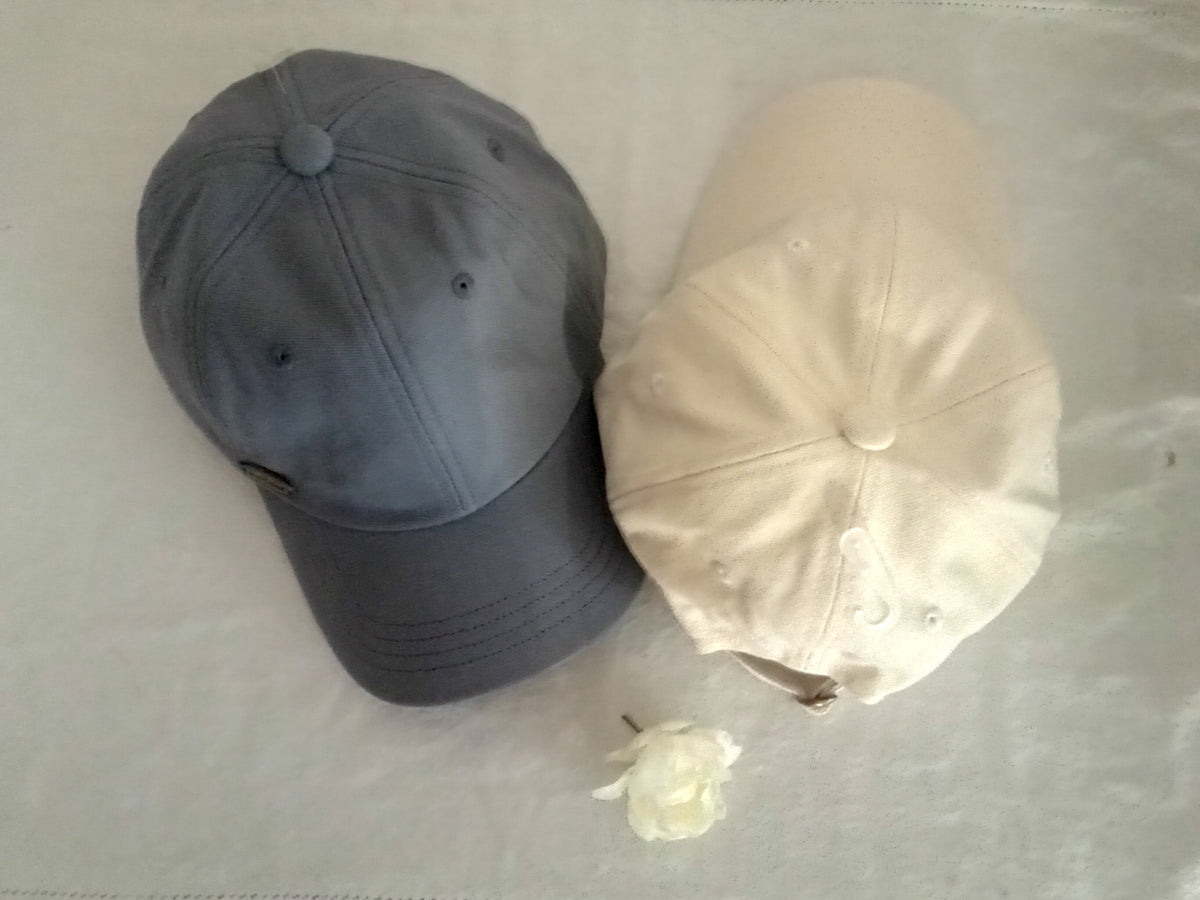 Two baseball caps, one gray and one beige, on a light surface.