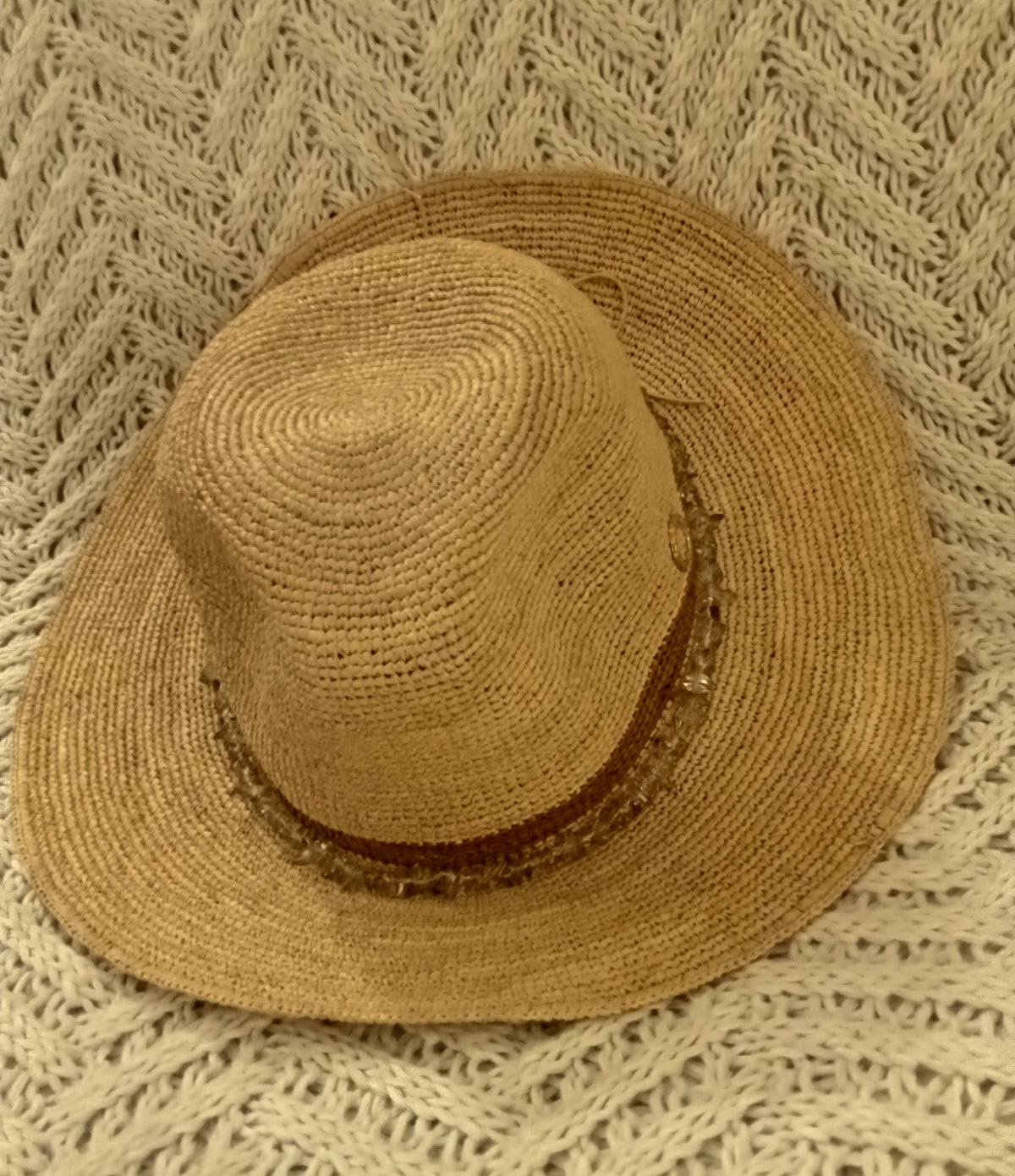 Brown straw hat with brown band and beads on a textured beige blanket.