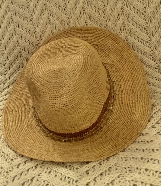 Brown straw hat with brown band and beads on a textured beige blanket.