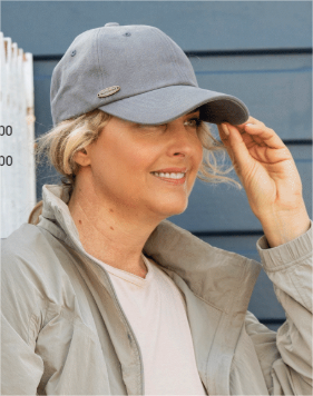 Woman wearing a washed-denim-blue cap and beige jacket against a blue wall.